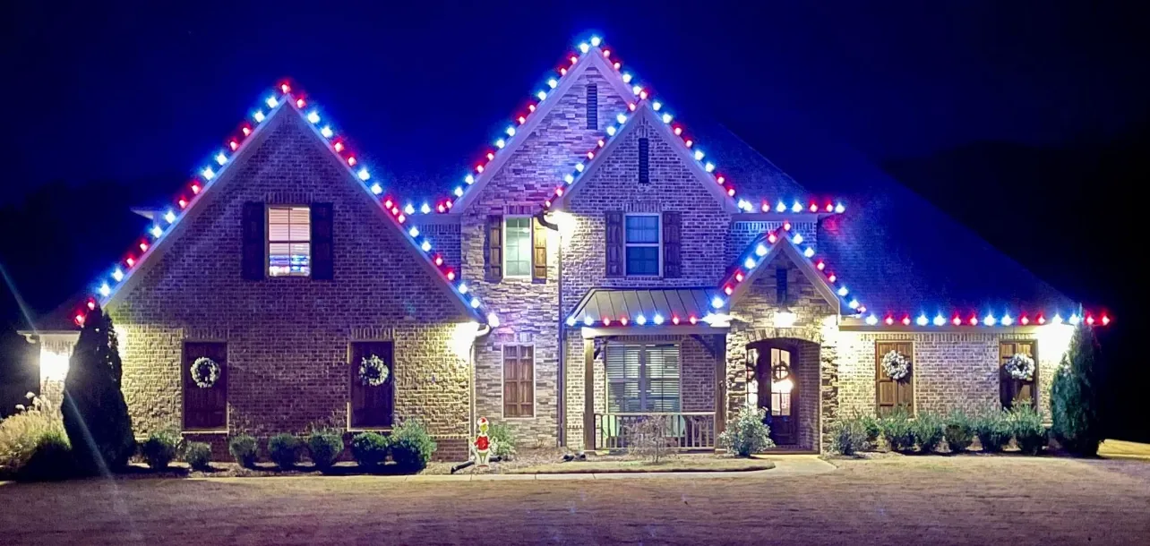 Brick home with red, white, and blue roofline lights at night