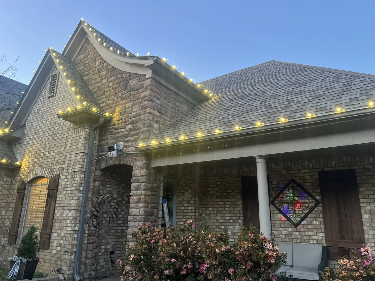Close-up of warm white C9 lights on a stone gable and porch roofline at dusk